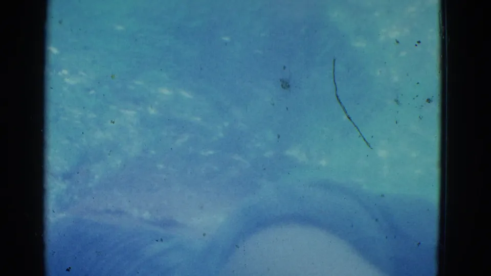 1953 8mm Yonkers home-movie frame showing pale blurred underwater forms in turquoise pool water with scratches, grain, and dust.