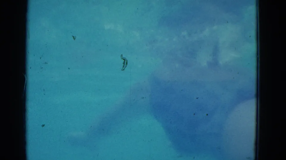 1953 8mm Yonkers underwater pool frame with turquoise water, blue shadowed forms, soft light, dust, scratches, and gate edges.