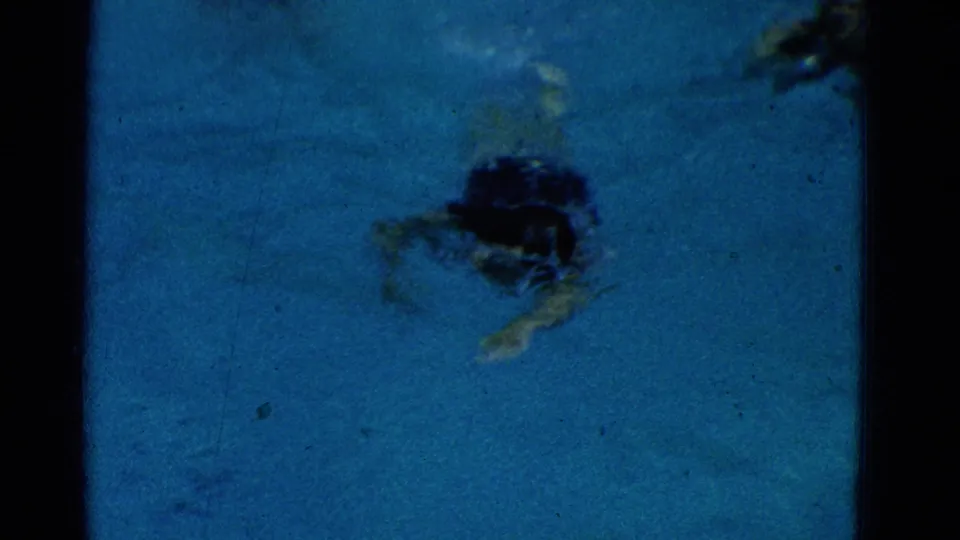 1953 Yonkers frame of a swimmer moving underwater in a community pool, seen through blue water with grain and scratches.