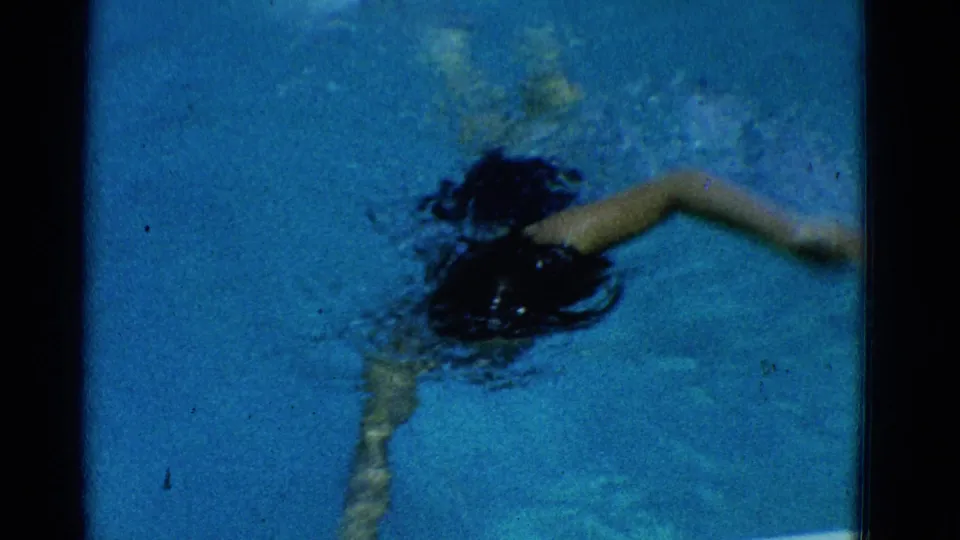 1953 Yonkers home-movie frame showing a swimmer underwater with one arm extended during a stroke in the pool.