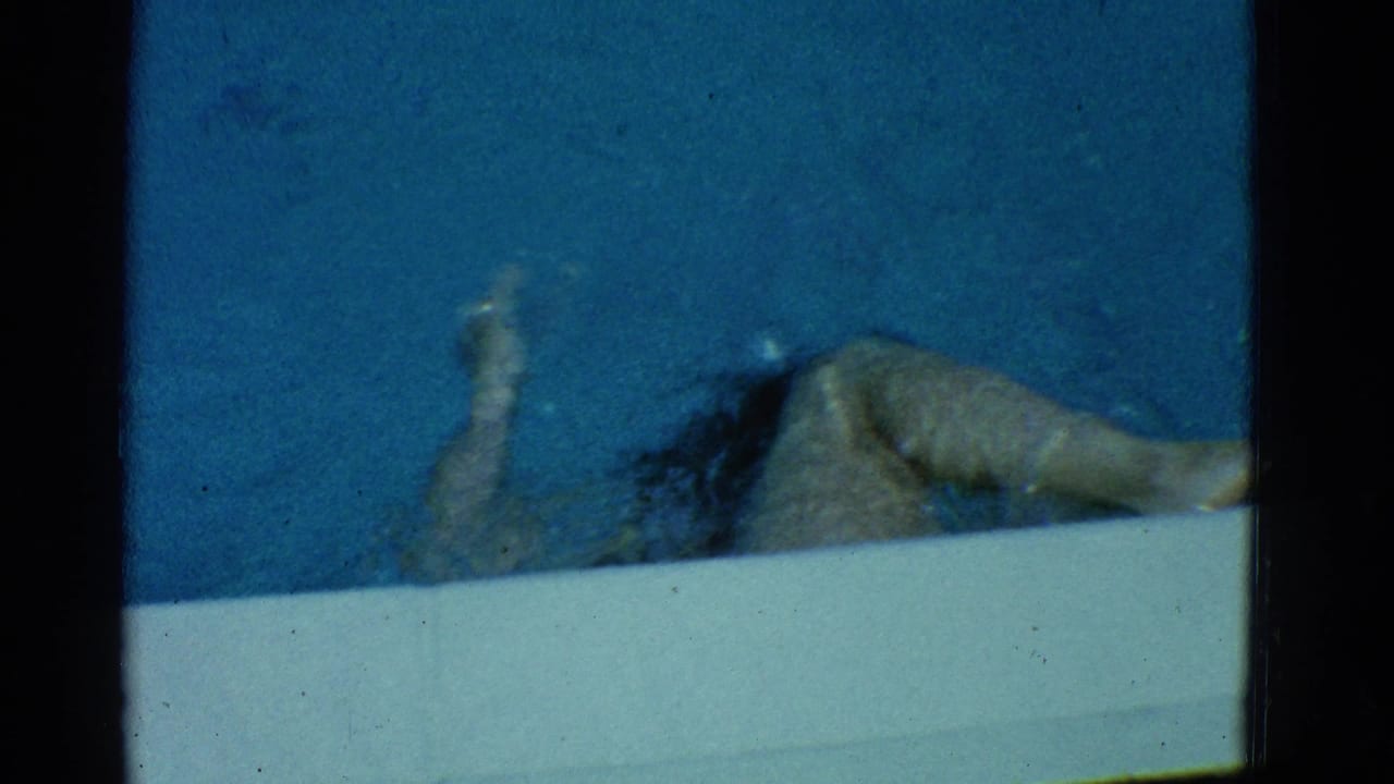 In 1953 Yonkers home-movie footage, a woman in a dark one-piece swimsuit swims near the edge of a blue pool.