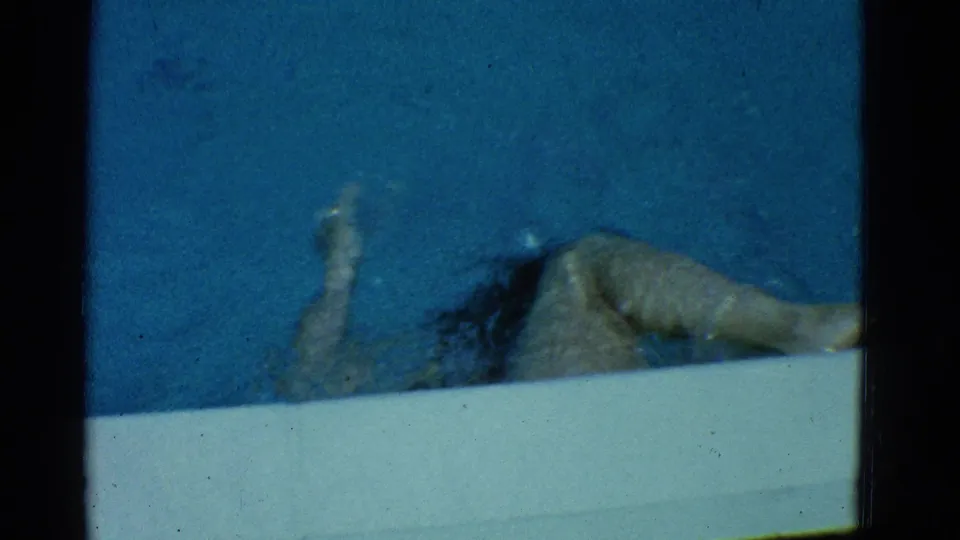 In 1953 Yonkers home-movie footage, a woman in a dark one-piece swimsuit swims near the edge of a blue pool.
