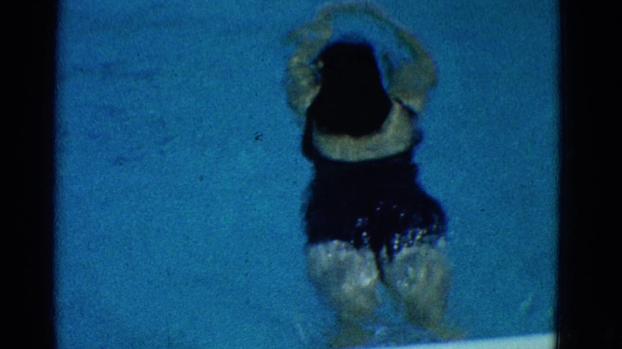 Woman seen from behind underwater with legs kicking in blue pool water.