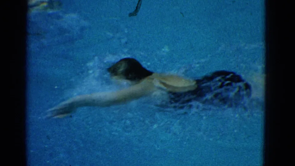 The swimmer performs a freestyle stroke underwater, one arm stretched ahead as bubbles and motion blur surround her.