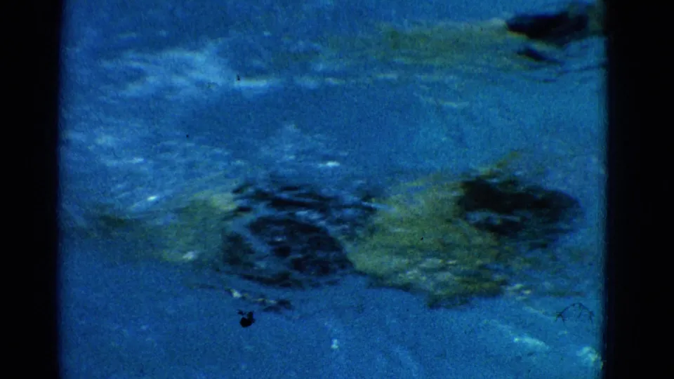 Archival 8mm frame from Yonkers showing a swimmer gliding underwater below rippled blue pool water.