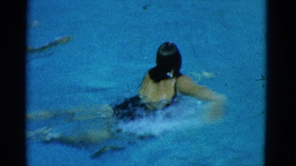 1953 home-movie frame in Yonkers showing a young swimmer from behind at the pool surface during a stroke.