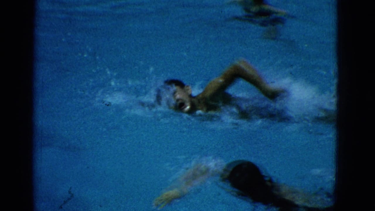 1953 Yonkers home-movie frame showing swimmers in a pool, including one swimmer mid-freestyle with splashing water.