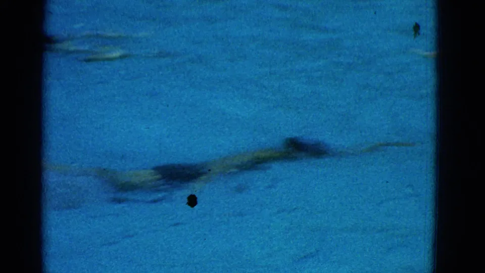 1953 Yonkers frame showing a swimmer stretched out in the pool, seen through soft 8mm motion blur and blue-tinted water.