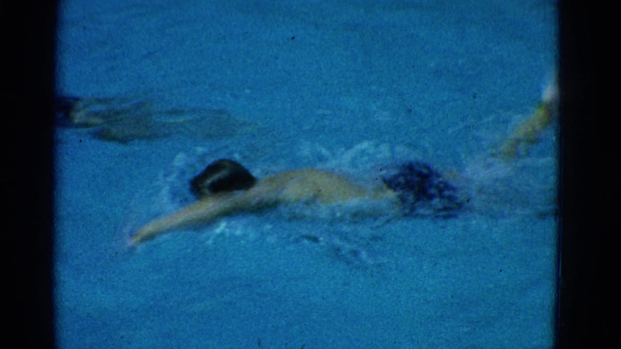 1953 Yonkers 8mm frame showing a male swimmer crossing a blue pool lane with motion blur and water splash.