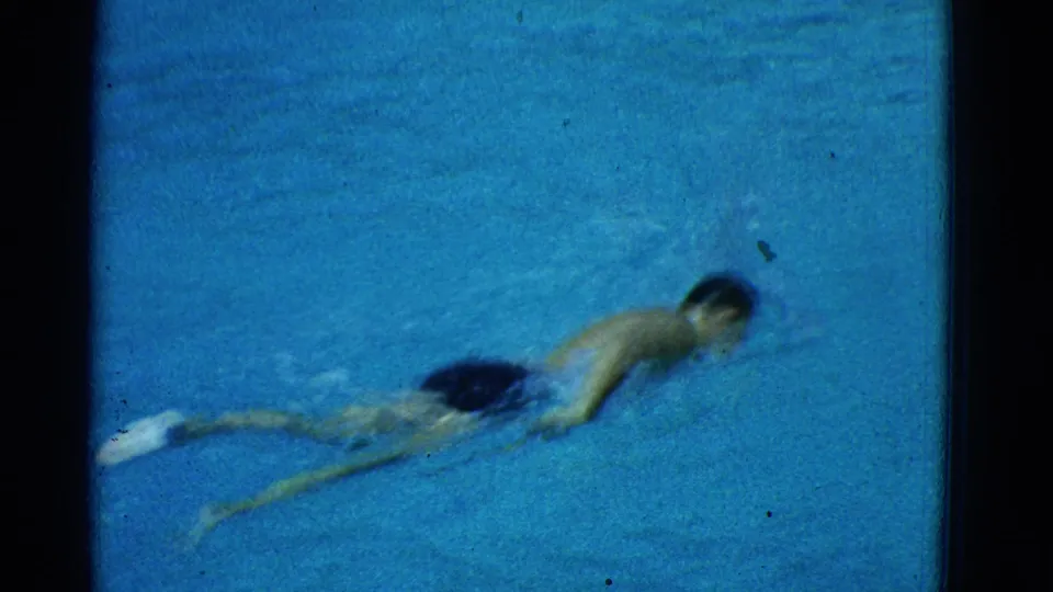 1953 Yonkers home-movie frame of a male swimmer continuing a lap through blue pool water.
