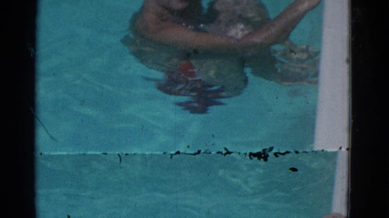 Man partly submerged in turquoise pool water with arms near the pool edge.