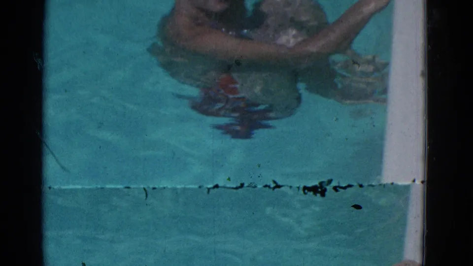 1953 Yonkers home-movie frame showing a man partly submerged in a pool, with reflections in turquoise water and visible film wear.