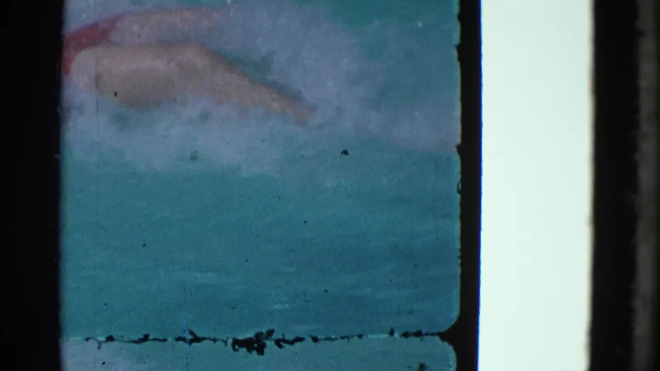 1953 Yonkers home-movie frame showing blue-green water, a faint submerged form, and worn 8mm frame edges.