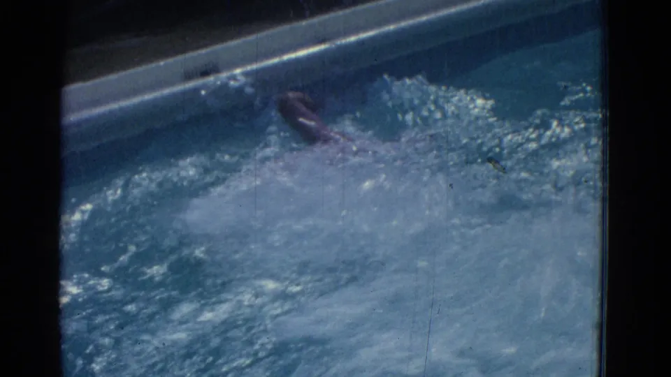 The swimmer's arm and shoulder surface near a pool edge in the 1953 Yonkers swimming footage, surrounded by splashes and ripples.