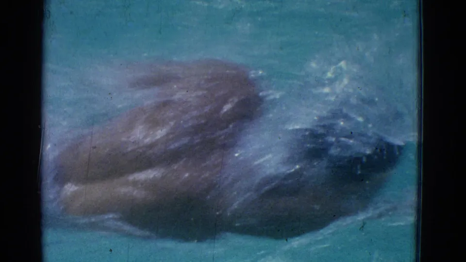 A swimmer in white swimwear is seen partly underwater in the 1953 Yonkers pool footage, with softened focus and blue-green water around them.