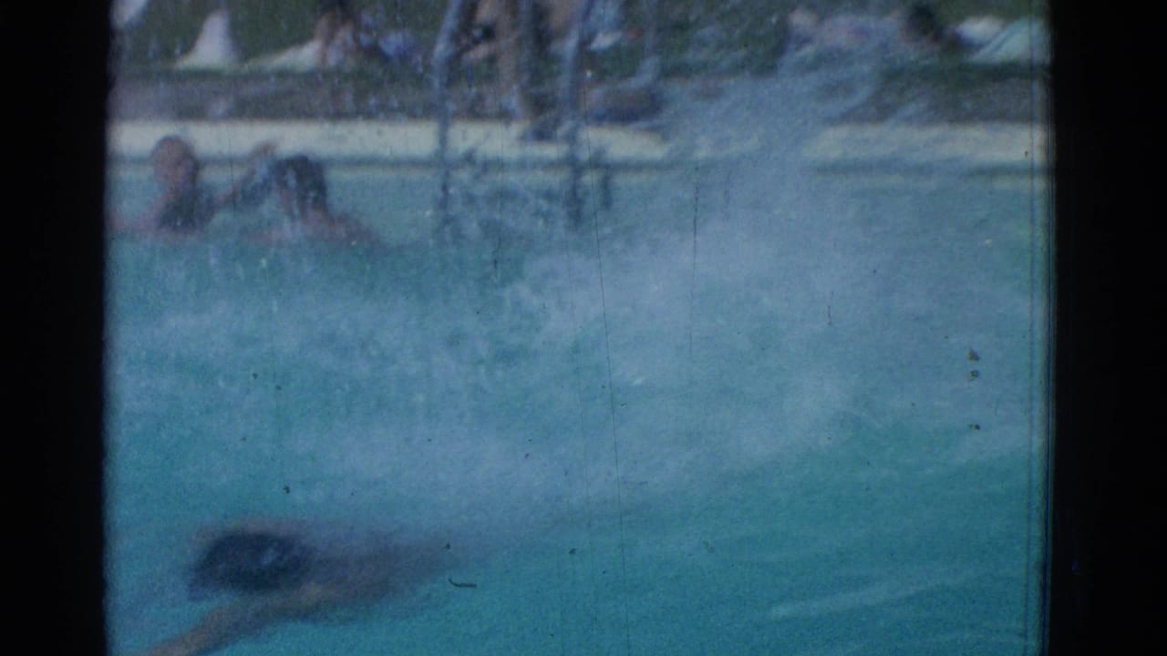 Swimmer in a dark cap moves through blue pool water near the left side of the frame.