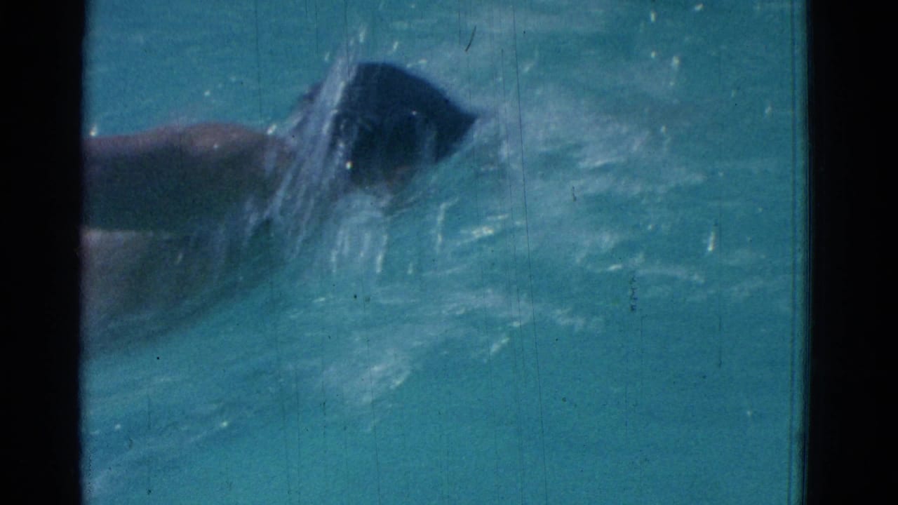 1953 Yonkers frame showing a swimmer in a dark swim cap cutting through turquoise pool water during a freestyle stroke.