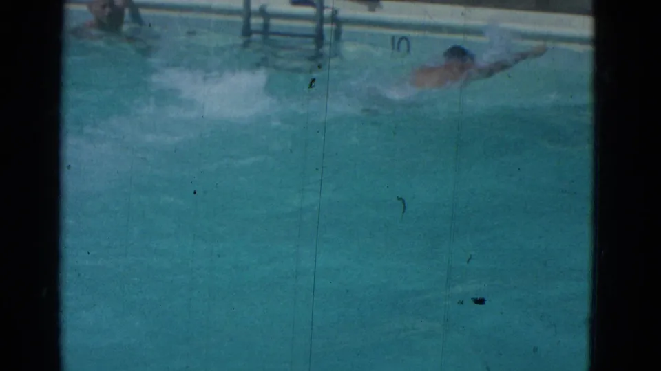 1953 Yonkers 8mm frame with a swimmer partly submerged, moving across the pool below a ladder and edge markings.