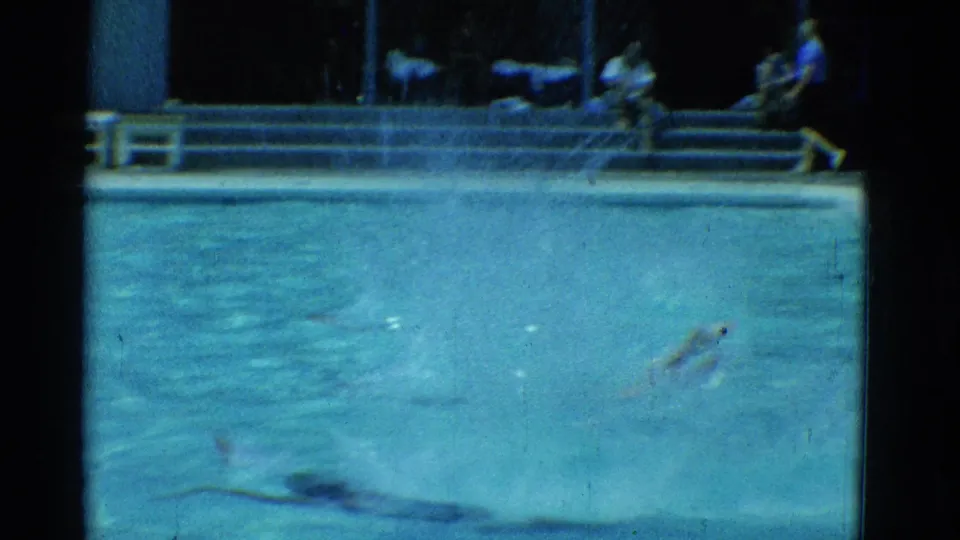 1953 Yonkers 8mm pool view showing the swimmer near the lower frame while distant seated figures appear along the far side.