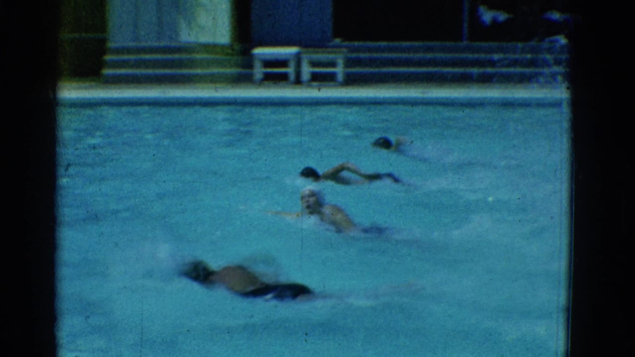 Four swimmers move across an outdoor pool with splashes and a deck behind them.
