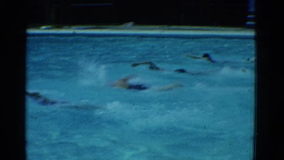 A 1953 Yonkers pool race continues, with swimmers low in the water and splashes filling the foreground of the 8mm frame.