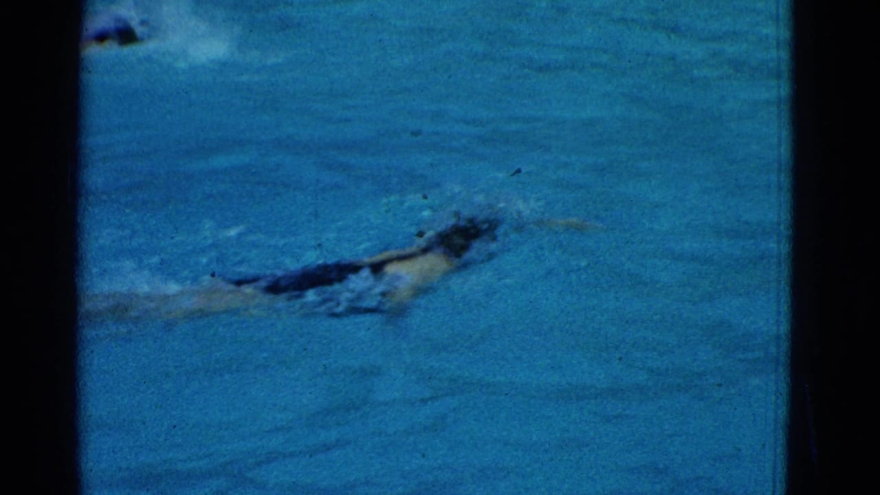 Swimmer moves across blue pool water in a dark cap and swimsuit.