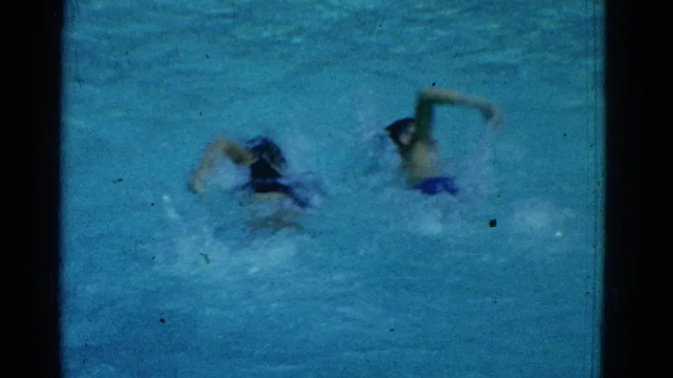 Two swimmers appear side by side in the Yonkers pool, with splashing water and soft 8mm color texture.