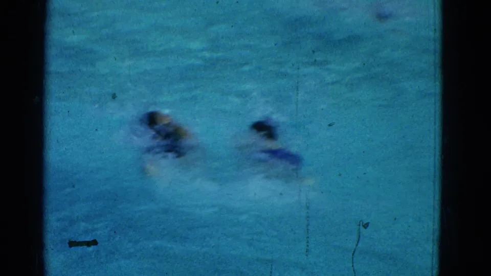 The final frame shows two swimmers continuing through the pool in soft, scratched 1953 8mm home-movie footage.
