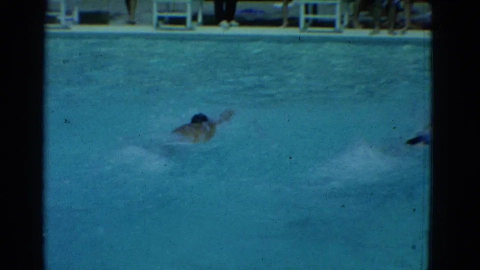 A swimmer continues freestyle through blue pool water in the 1953 Yonkers home-movie scene.