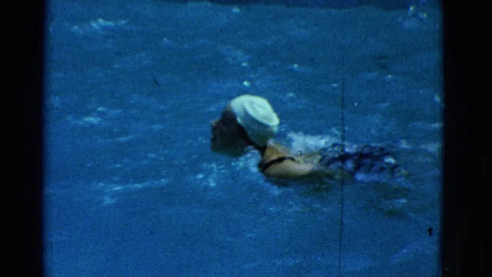 1953 Yonkers home-movie still showing the swimmer mid-lap, with cap and shoulder visible above the water.
