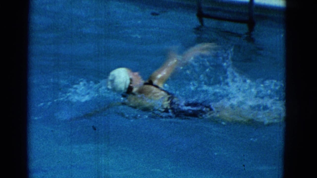 1953 Yonkers 8mm frame of a swimmer in a white cap and dark suit moving through a blue pool with splashing water.