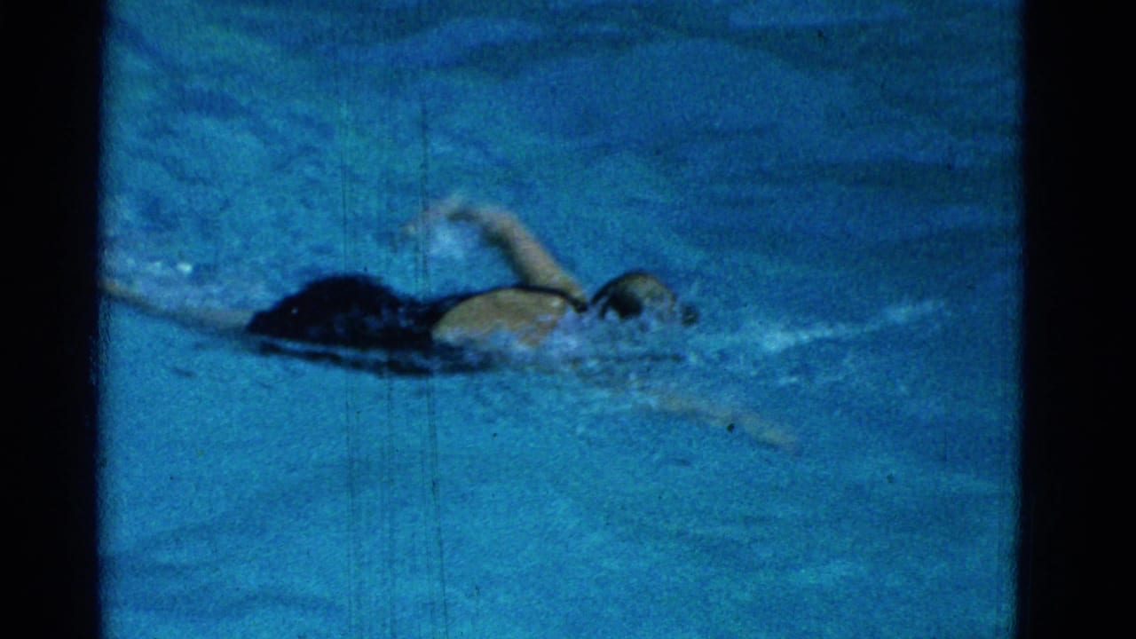 Swimmer in a dark cap crossing the pool with one arm raised.