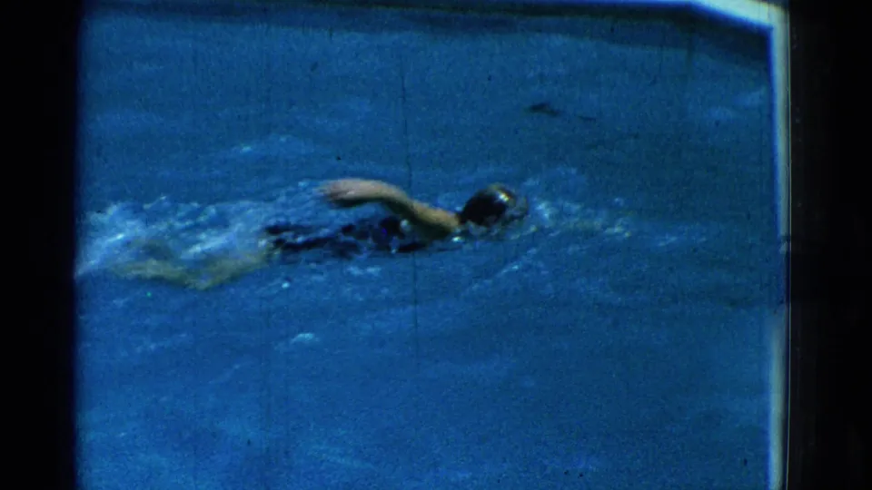 1953 Yonkers pool frame showing the swimmer farther from camera, continuing freestyle across blue water with visible wake and film wear.