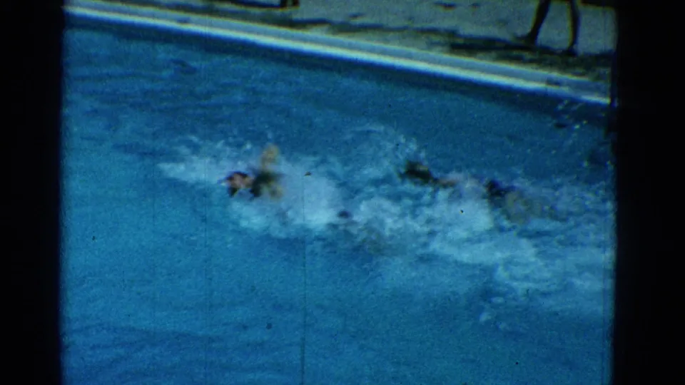 1953 Yonkers poolside frame showing swimmers practicing in a residential pool, with strong splashes and the far coping visible.