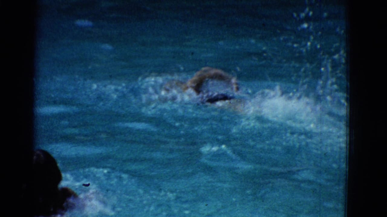1953 Yonkers home-movie frame showing swimmers in a pool, one partly submerged in the foreground and another splashing ahead.