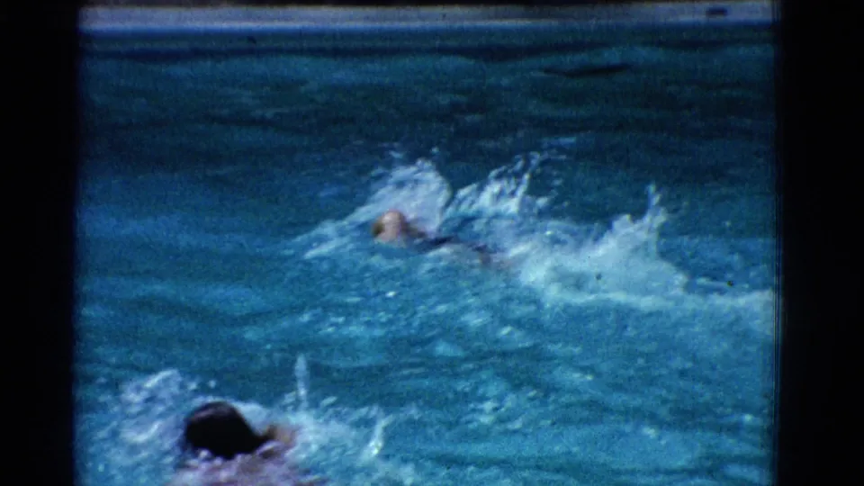 1953 Yonkers pool footage showing swimmers moving across the water near a concrete edge, with heavy splash and soft 8mm detail.