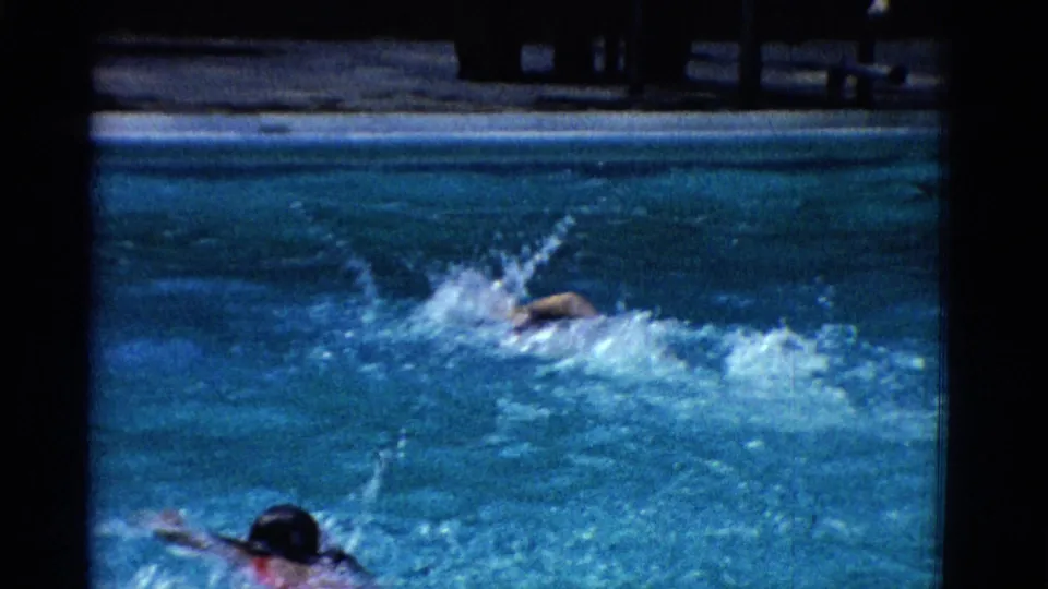 Home-movie frame from Yonkers in 1953 showing a swimmer overtaking through splashing water, with another swimmer partly visible below.