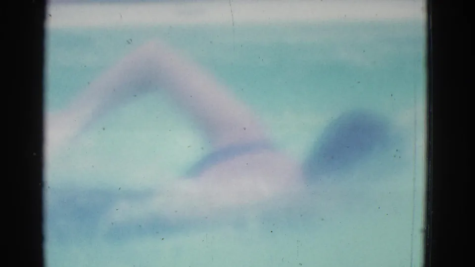1953 home-movie pool frame showing an indistinct swimmer form moving through blue-green water.