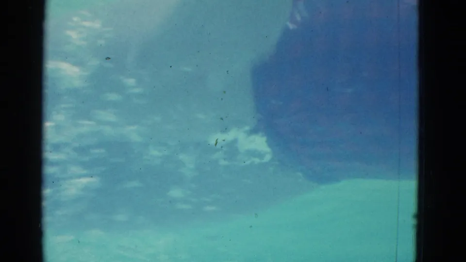 Underwater 1953 Yonkers pool frame showing a swimmer near the pool floor, softened by ripples and vintage 8mm texture.