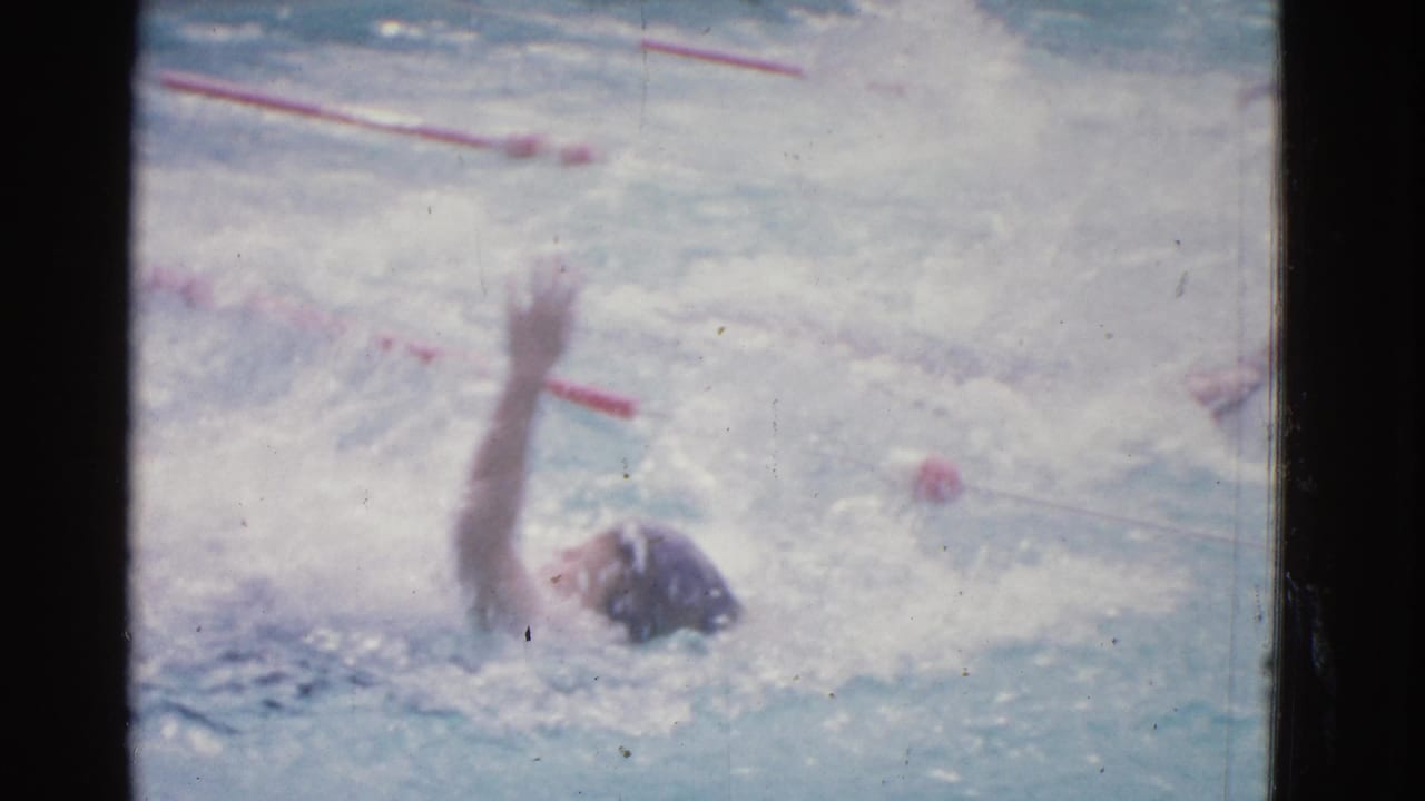 1953 Yonkers pool footage shows a swimmer on their back with one arm raised during a backstroke lap amid splashing water.