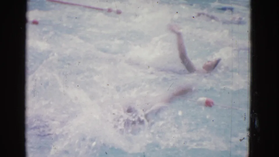 1953 Yonkers pool footage shows backstroke swimmers partly obscured by spray, with red lane dividers visible across the water.