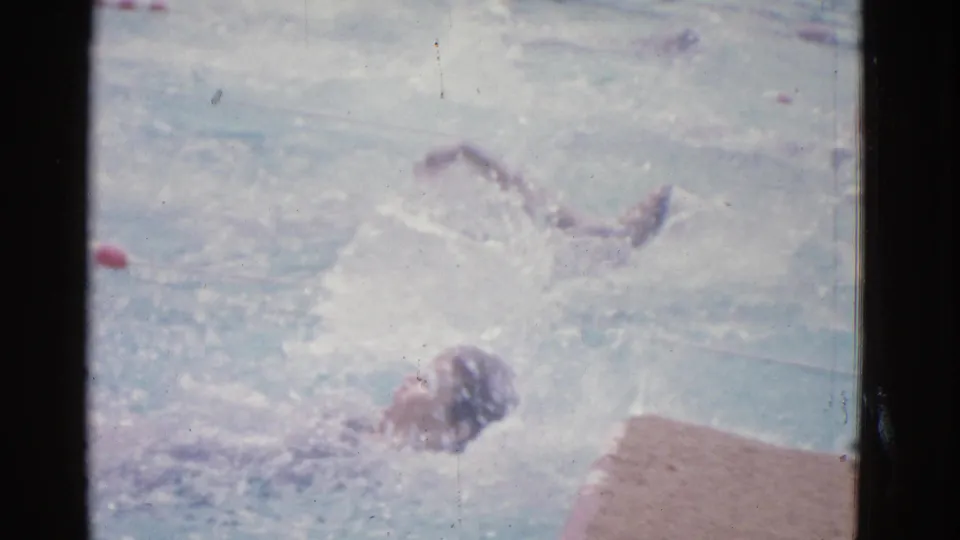1953 Yonkers pool footage shows a swimmer moving on their back near the pool deck, with another swimmer partly visible beyond the lane.