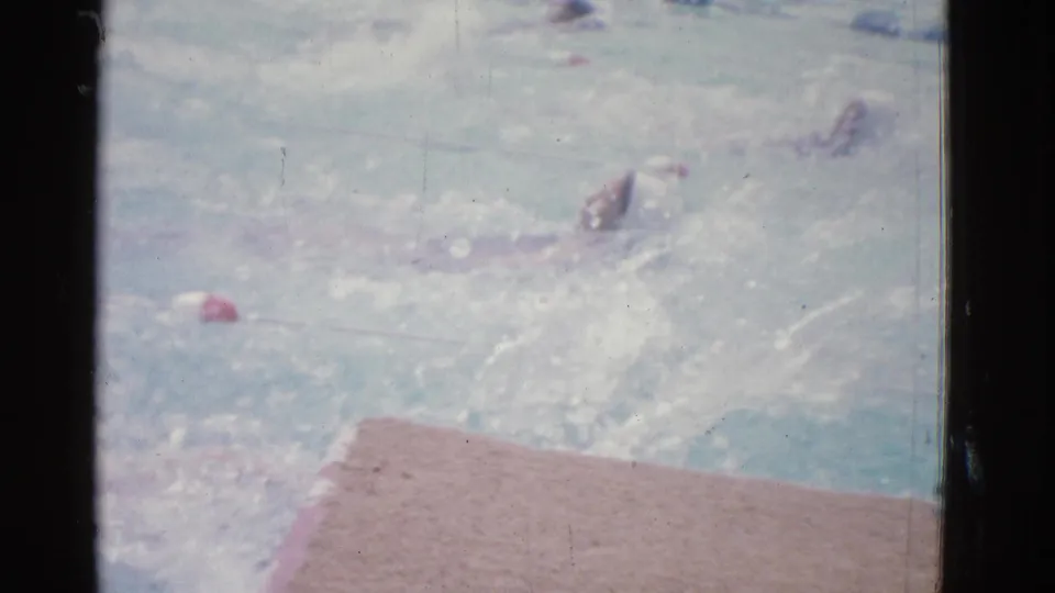 1953 Yonkers pool footage shows a swimmer completing a backstroke motion near the deck, with another swimmer faintly visible in the lane.