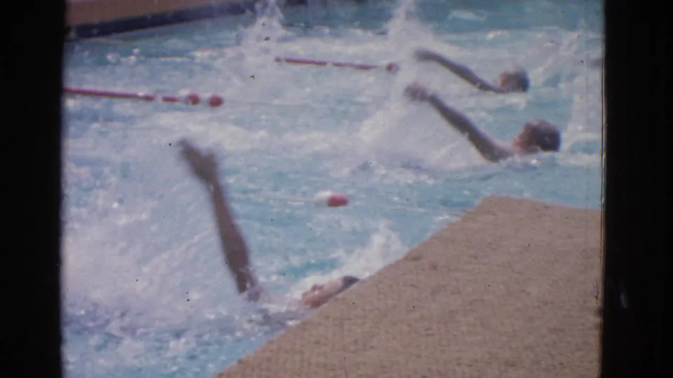 Young men swim backstroke in a Yonkers pool, with red lane markers and bright splashes visible in the 8mm frame.