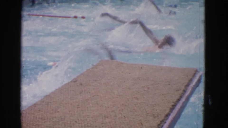 Poolside 8mm view of backstroke swimmers in Yonkers, with the textured deck filling the foreground and splashes across the lanes.
