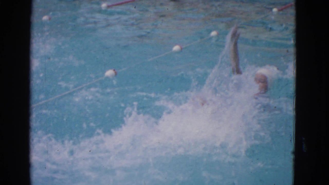 1953 Yonkers swim-school footage shows a capped swimmer partly submerged while practicing a freestyle stroke in a marked pool lane.