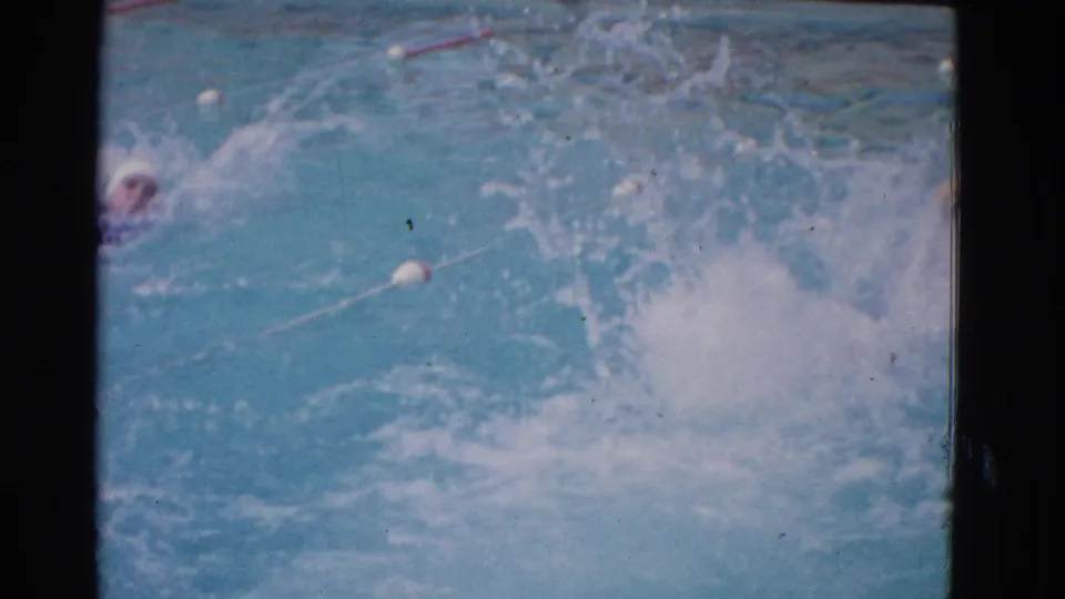 A capped swimmer advances through turquoise water in the 1953 Yonkers pool scene, with lane floats and spray visible around the stroke.