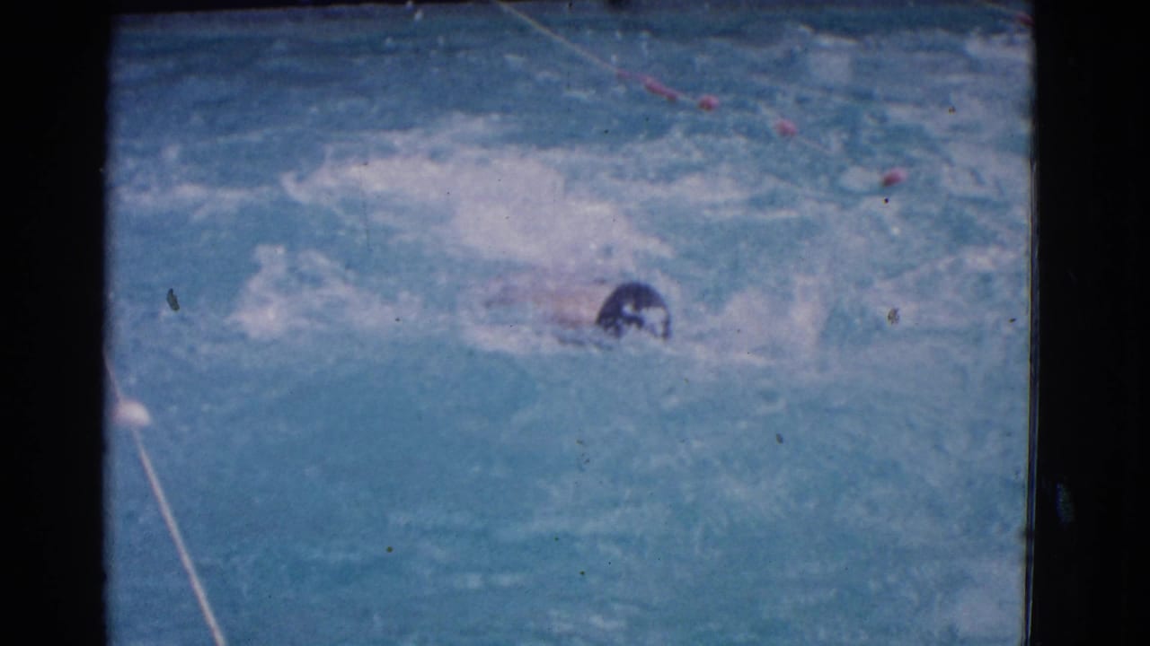 1953 Yonkers 8mm frame showing a male swimmer on his back in blue pool water with lane markers and visible film borders.