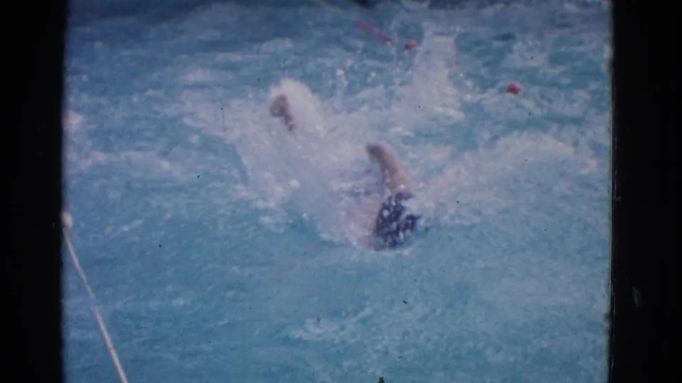 1953 Yonkers 8mm frame with a male swimmer rotating through backstroke, one arm raised amid bright pool splashes.