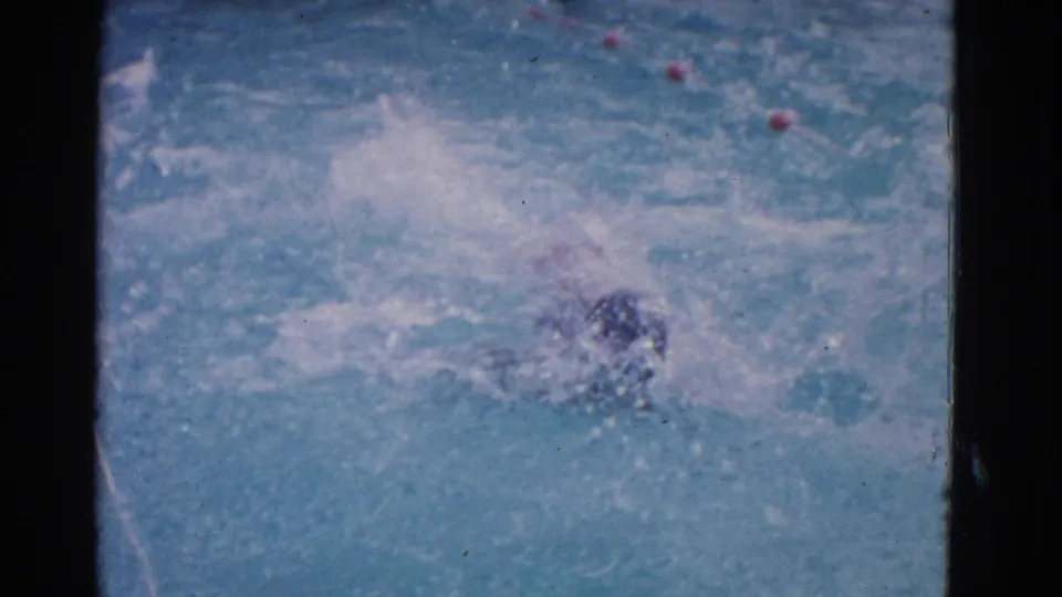 1953 Yonkers 8mm frame showing the swimmer partly submerged during backstroke, surrounded by ripples, splash, and lane markers.